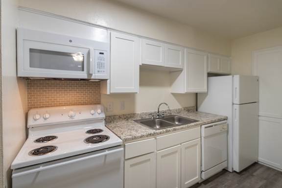 Kitchen with white cabinets and appliances in a 1 bedroom, 1 bath 752 sq ft apartment home with hardwoodlike flooring throughout at The Biltmore Apartments located in the Vickery Midtown neighborhood of Dallas, TX.