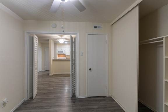 View of the dining area and kitchen beyond from the den containing a closet with built-in shelving in a 1 bedroom, 1 bath 752 sq ft apartment home with hardwoodlike flooring throughout at The Biltmore Apartments located in the Vickery Midtown neighborhood of Dallas, TX.