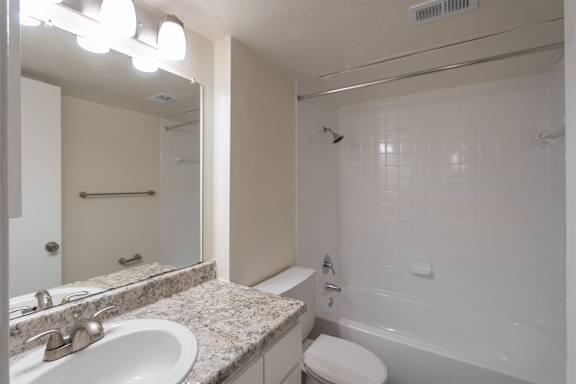 Bathroom with white vanity and tub surround in a 1 bedroom, 1 bath 752 sq ft apartment home with hardwoodlike flooring throughout at The Biltmore Apartments located in the Vickery Midtown neighborhood of Dallas, TX.