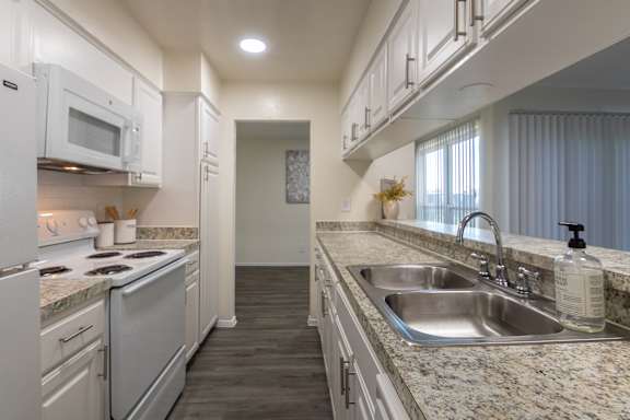 Kitchen with white cabinets and white appliances and large pass-through window in a 2 bedroom, 1.5 bath 1084 sq ft, 2-floor townhome at The Biltmore Apartments located in the Vickery Midtown neighborhood of Dallas, TX.