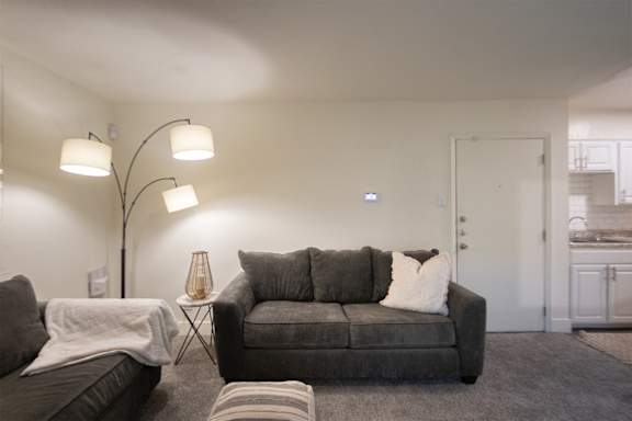A living room with a grey couch and a floor lamp in a 1 bedroom, 1 bath 554 sq ft apartment home at The Biltmore Apartments located in the Vickery Midtown neighborhood of Dallas, TX.