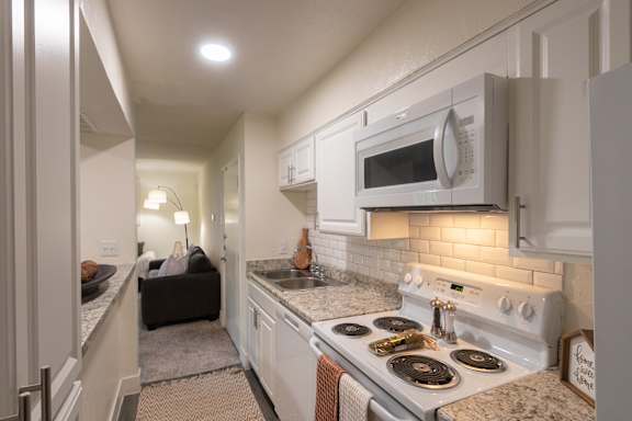 A kitchen with white appliances and white cabinets in a 1 bedroom, 1 bath 554 sq ft apartment home at The Biltmore Apartments located in the Vickery Midtown neighborhood of Dallas, TX.