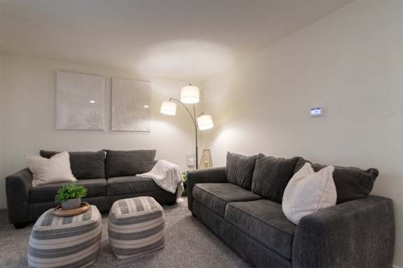 A living room with grey couches and striped ottomans in a 1 bedroom, 1 bath 554 sq ft apartment home at The Biltmore Apartments located in the Vickery Midtown neighborhood of Dallas, TX.