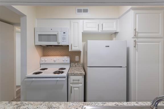 Kitchen with white cabinets and white appliances in a 2 bedroom, 1.5 bath 846 sq ft apartment home at The Biltmore Apartments located in the Vickery Midtown neighborhood of Dallas, TX.
