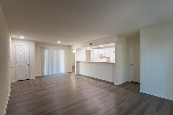 A kitchen with white appliances and cabinets with hardwoodlike flooring throughout viewed from the living room in a 2 bedroom, 2 bath 991 sq ft apartment home at The Biltmore Apartments located in the Vickery Midtown neighborhood of Dallas, TX.