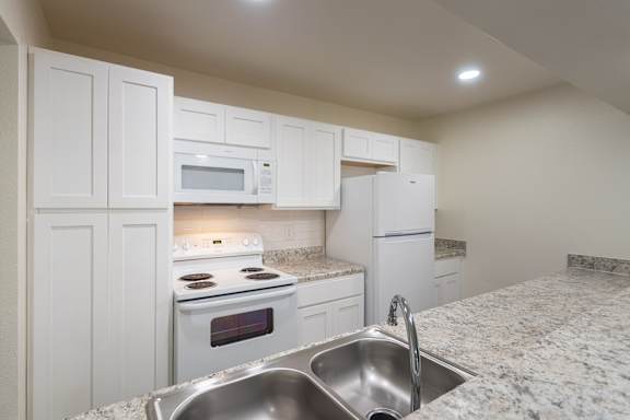 A kitchen with white appliances and cabinets with hardwoodlike flooring throughout in a 2 bedroom, 2 bath 991 sq ft apartment home at The Biltmore Apartments located in the Vickery Midtown neighborhood of Dallas, TX.
