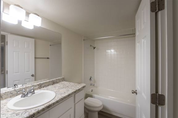 A bathroom with white vanity with hardwoodlike flooring throughout in a 2 bedroom, 2 bath 991 sq ft apartment home at The Biltmore Apartments located in the Vickery Midtown neighborhood of Dallas, TX.