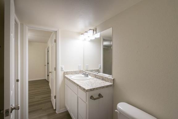 A bathroom with white vanity with hardwoodlike flooring throughout in a 2 bedroom, 2 bath 991 sq ft apartment home at The Biltmore Apartments located in the Vickery Midtown neighborhood of Dallas, TX.