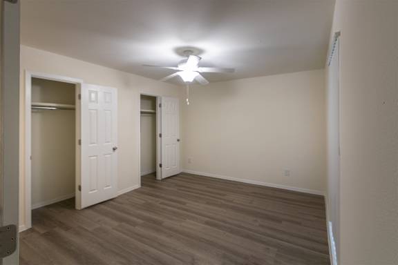 A bedroom with white ceiling fan  with white vanity with hardwoodlike flooring throughoutin a 2 bedroom, 2 bath 991 sq ft apartment home at The Biltmore Apartments located in the Vickery Midtown neighborhood of Dallas, TX.