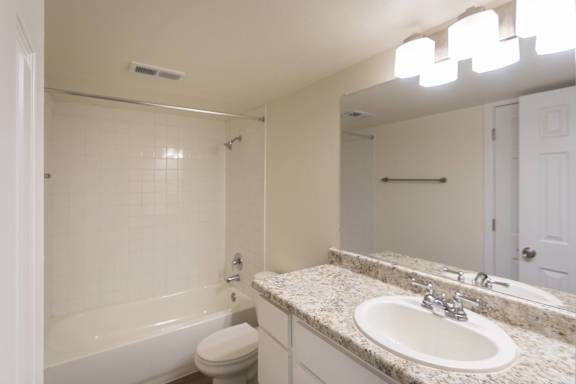 Primary bathroom with white vanity with white vanity with hardwoodlike flooring throughout in a 2 bedroom, 2 bath 991 sq ft apartment home at The Biltmore Apartments located in the Vickery Midtown neighborhood of Dallas, TX.