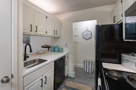 Kitchen in a 1-bedroom apartment at Cambridge Court Apartments in Dallas, Texas, featuring white cabinetry, black appliances, sink, and counter space.