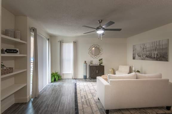 Living room in a 1-bedroom apartment at Cambridge Court Apartments in Dallas, Texas, showing wood-style flooring, a patio door, built-in shelving, and staged seating.