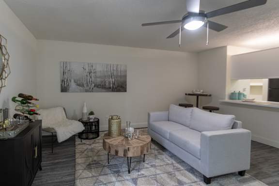 Staged living room in a 1-bedroom apartment at Cambridge Court Apartments in Dallas, Texas, featuring wood-style flooring, neutral walls, ceiling fan, and open connection to the kitchen.