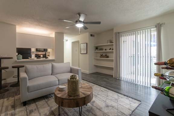 Living room view in a 1-bedroom apartment at Cambridge Court Apartments in Dallas, Texas, showing staged seating, wood-style flooring, patio door, and connection to the kitchen.