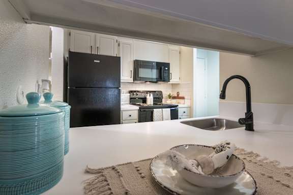 Breakfast bar and kitchen view in a 1-bedroom apartment at Cambridge Court Apartments in Dallas, Texas, showing counter seating, sink, black appliances, and open connection to the living area. Title: Cambridge Court Breakfast Bar and Kitchen
