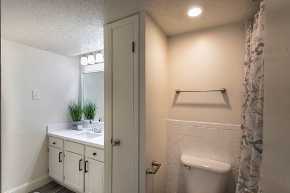 Bathroom in a 1-bedroom apartment at Cambridge Court Apartments in Dallas, Texas, showing vanity storage, mirror, toilet, towel bar, and tub/shower area.