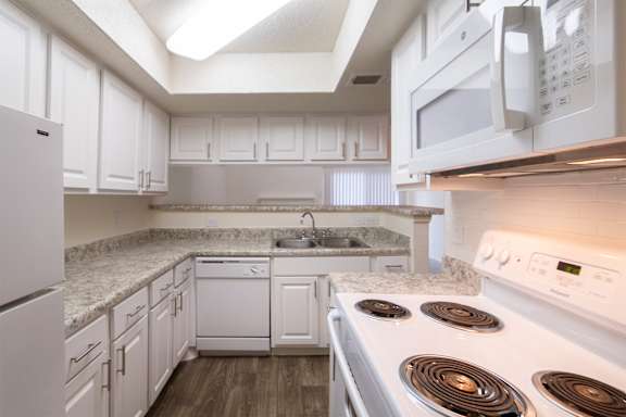 A kitchen with white cabinets and appliances in a 717 square foot 1 bedroom, 1 bath loft apartment home at Canyon Creek Apartments in Dallas Midtown neighborhood of Dallas, TX.