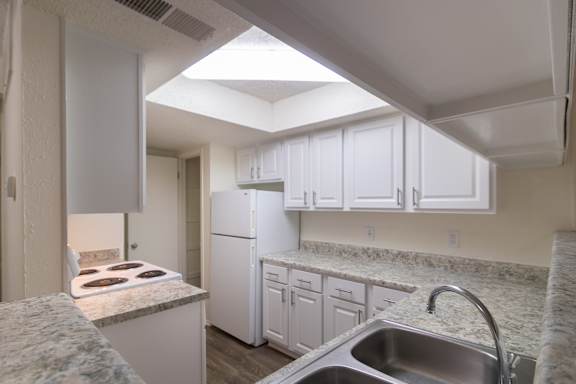 A kitchen with white cabinets and appliances in a 717 square foot 1 bedroom, 1 bath loft apartment home at Canyon Creek Apartments in Dallas Midtown neighborhood of Dallas, TX.