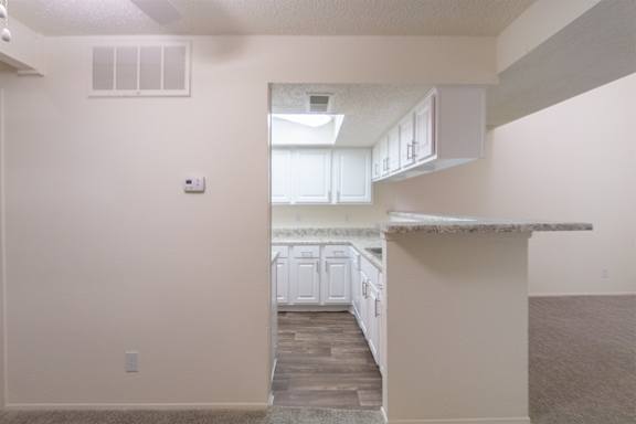 View of the kitchen with white cabinets and appliances from the dining room of a 717 square foot 1 bedroom, 1 bath loft apartment home at Canyon Creek Apartments in Dallas Midtown neighborhood of Dallas, TX.