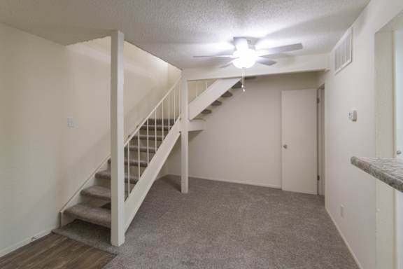 A dining room with white a ceiling fan and staircase to the second floor bedroom in a 717 square foot 1 bedroom, 1 bath loft apartment home at Canyon Creek Apartments in Dallas Midtown neighborhood of Dallas, TX.
