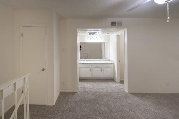 A view of the bathroom with a large white vanity from the bedroom in a 717 square foot 1 bedroom, 1 bath loft apartment home at Canyon Creek Apartments in Dallas Midtown neighborhood of Dallas, TX.