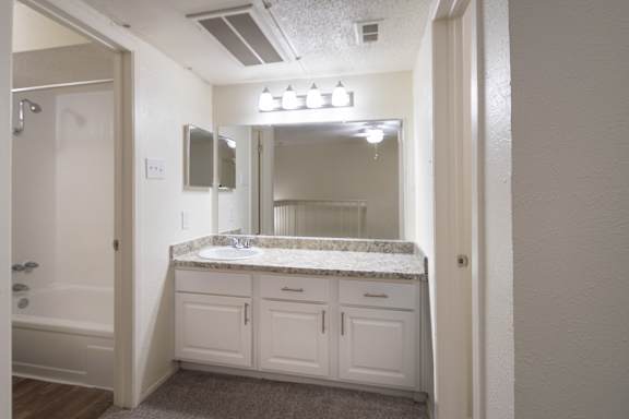 A bathroom with a large white vanity in the bedroom in a 717 square foot 1 bedroom, 1 bath loft apartment home at Canyon Creek Apartments in Dallas Midtown neighborhood of Dallas, TX.