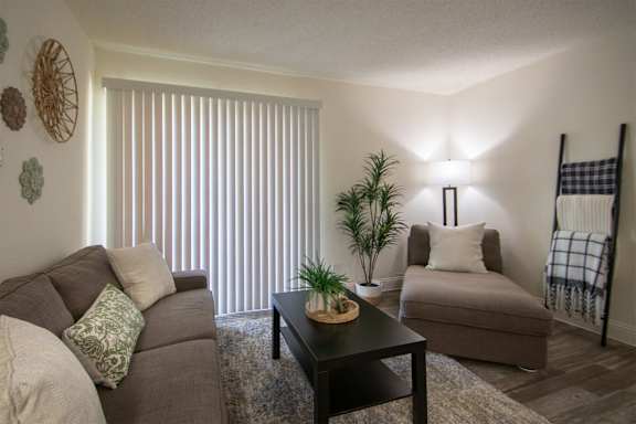 Living room with a couch, chaise lounge and a potted plant in a 515 square foot 1 bedroom, 1 bath apartment home at Canyon Creek Apartments in Dallas Midtown neighborhood of Dallas, TX.