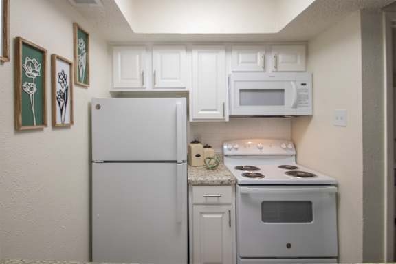 A kitchen with a white cabinets and appliances in a 515 square foot 1 bedroom, 1 bath apartment home at Canyon Creek Apartments in Dallas Midtown neighborhood of Dallas, TX.