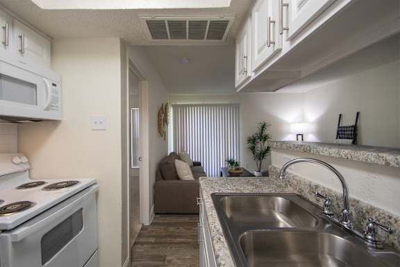 A kitchen with a white cabinets and appliances in a 515 square foot 1 bedroom, 1 bath apartment home at Canyon Creek Apartments in Dallas Midtown neighborhood of Dallas, TX.