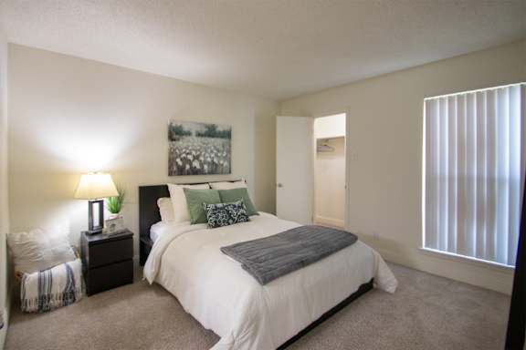 A bedroom with a large bed and a painting on the wall in a 515 square foot 1 bedroom, 1 bath apartment home at Canyon Creek Apartments in Dallas Midtown neighborhood of Dallas, TX.
