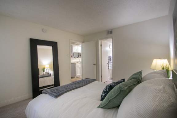 A bedroom with a large painting and a large mirror leaning against the wall in a 515 square foot 1 bedroom, 1 bath apartment home at Canyon Creek Apartments in Dallas Midtown neighborhood of Dallas, TX.