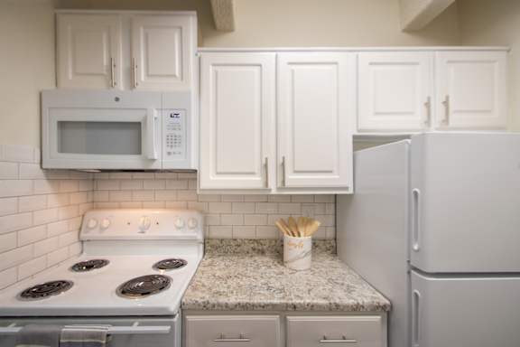 A kitchen with white cabinets and white appliances in a 1 bedroom, 1 bath apartment home at Harvard Square Apartments in the Vickery Midtown neighborhood of Dallas, TX.