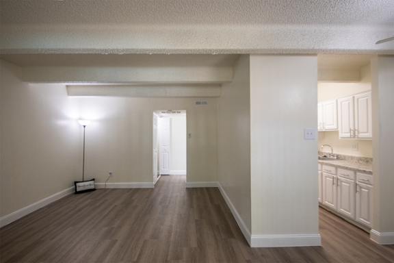 A living room looking into the kitchen through the dining area with hardwoodlike flooring throughout in a 1 bedroom, 1 bath apartment home at Harvard Square Apartments in the Vickery Midtown neighborhood of Dallas, TX.