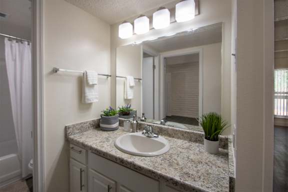 A bathroom and white bath vanity with hardwoodlike flooring in a 1 bedroom, 1 bath apartment home at Harvard Square Apartments in the Vickery Midtown neighborhood of Dallas, TX.
