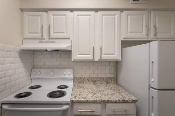 A kitchen with a white cabinets and a white appliances in a 2 bedroom, 1 bath apartment home at Harvard Square Apartments in the Vickery Midtown neighborhood of Dallas, TX.