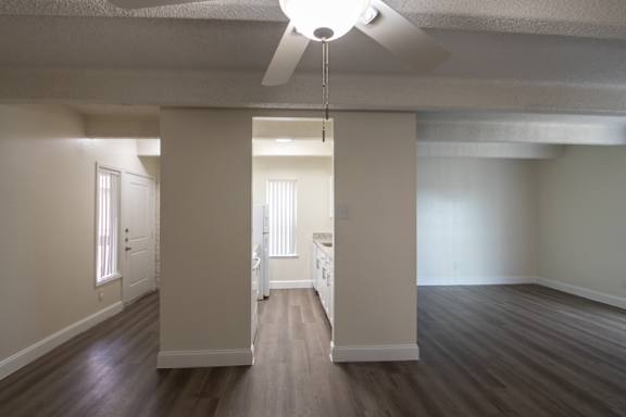 A view from the dining room with white ceiling fan looking towards the kitchen and entryway with hardwoodlike flooring throughout in a 2 bedroom, 2 bath with balcony apartment home at Harvard Square Apartments in the Vickery Midtown neighborhood of Dallas, TX.