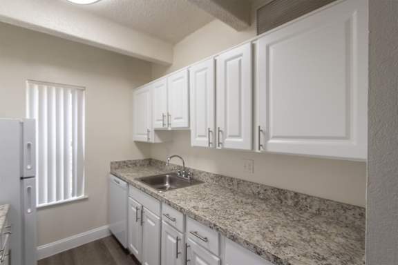 A kitchen with white cabinets and white appliances in a 2 bedroom, 2 bath with balcony apartment home at Harvard Square Apartments in the Vickery Midtown neighborhood of Dallas, TX.