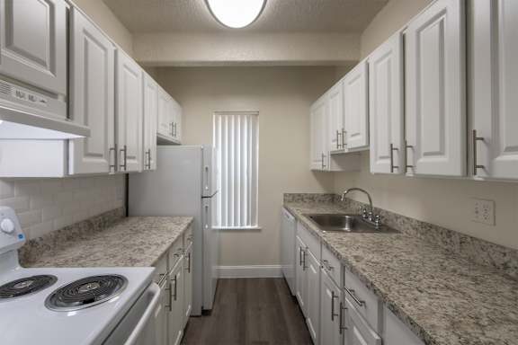 A kitchen with white cabinets and white appliances in a 2 bedroom, 2 bath with balcony apartment home at Harvard Square Apartments in the Vickery Midtown neighborhood of Dallas, TX.