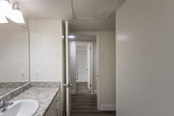 A view from the primary bathroom to a bathroom across the hallway in a 2 bedroom, 2 bath with balcony apartment home at Harvard Square Apartments in the Vickery Midtown neighborhood of Dallas, TX.