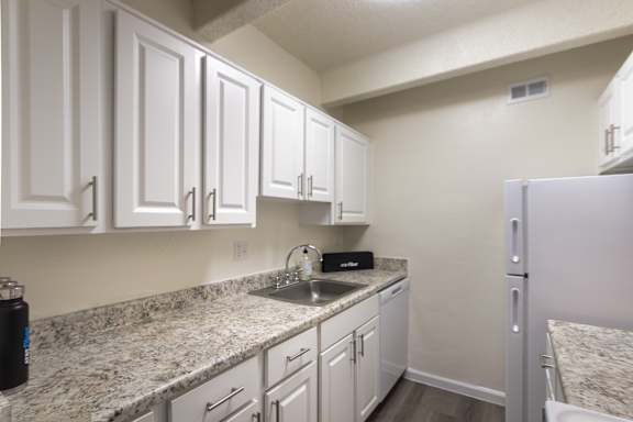Galley kitchen with white cabinets, granite-style countertops, and full-size refrigerator in a 653-square-foot apartment home