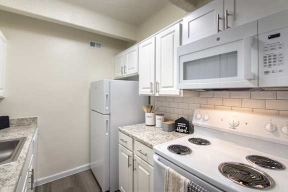 Kitchen with white cabinetry, electric range, and tile backsplash in a one-bedroom apartment at Harvard Square Apartments