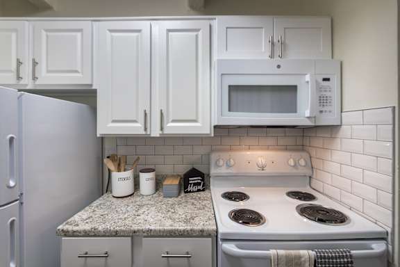Kitchen with white cabinets, microwave, and granite-style countertops in a 653-square-foot one-bedroom apartment