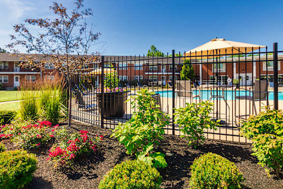 Pool entrance with black fencing, flowers, and umbrella-covered seating at Lake of the Woods Apartments