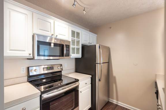 Kitchen appliance wall in the Catamaran 1-bedroom apartment, with white cabinetry, microwave, range, refrigerator, and wood-style flooring.