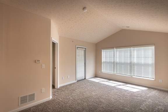 Living room in the Catamaran apartment, with a large window, patio door, carpeted flooring, and open space for seating or dining.