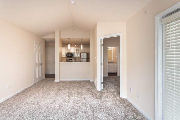 Living area in the Catamaran 1-bedroom apartment at Nantucket Apartments, with carpeted flooring, patio door, kitchen pass-through, and bathroom access nearby.