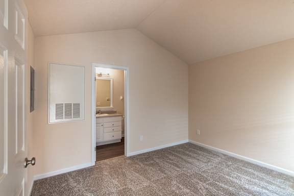 Bedroom view in the Catamaran apartment, with carpeted flooring, neutral walls, closet access, and the bathroom vanity visible beyond.
