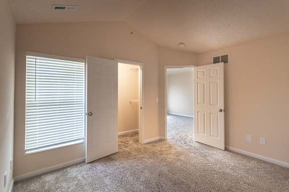 Bedroom in the Catamaran 1-bedroom apartment at Nantucket Apartments, with carpeted flooring, window blinds, and doorways leading toward the closet and bathroom.