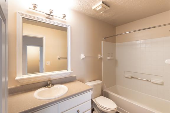 A Bathroom in the Catamaran apartment at Nantucket Apartments, with a vanity, mirror, toilet, and tub/shower combination. with a toilet, sink, and bathtub.
