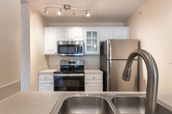 Kitchen view in the Catamaran apartment at Nantucket Apartments, looking past the sink toward the range, microwave, refrigerator, and white cabinets.